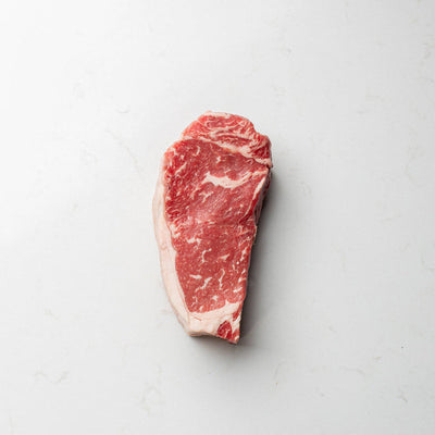 A close-up view of a fresh, local, and natural New York striploin steak, displayed at the butcher shoppe