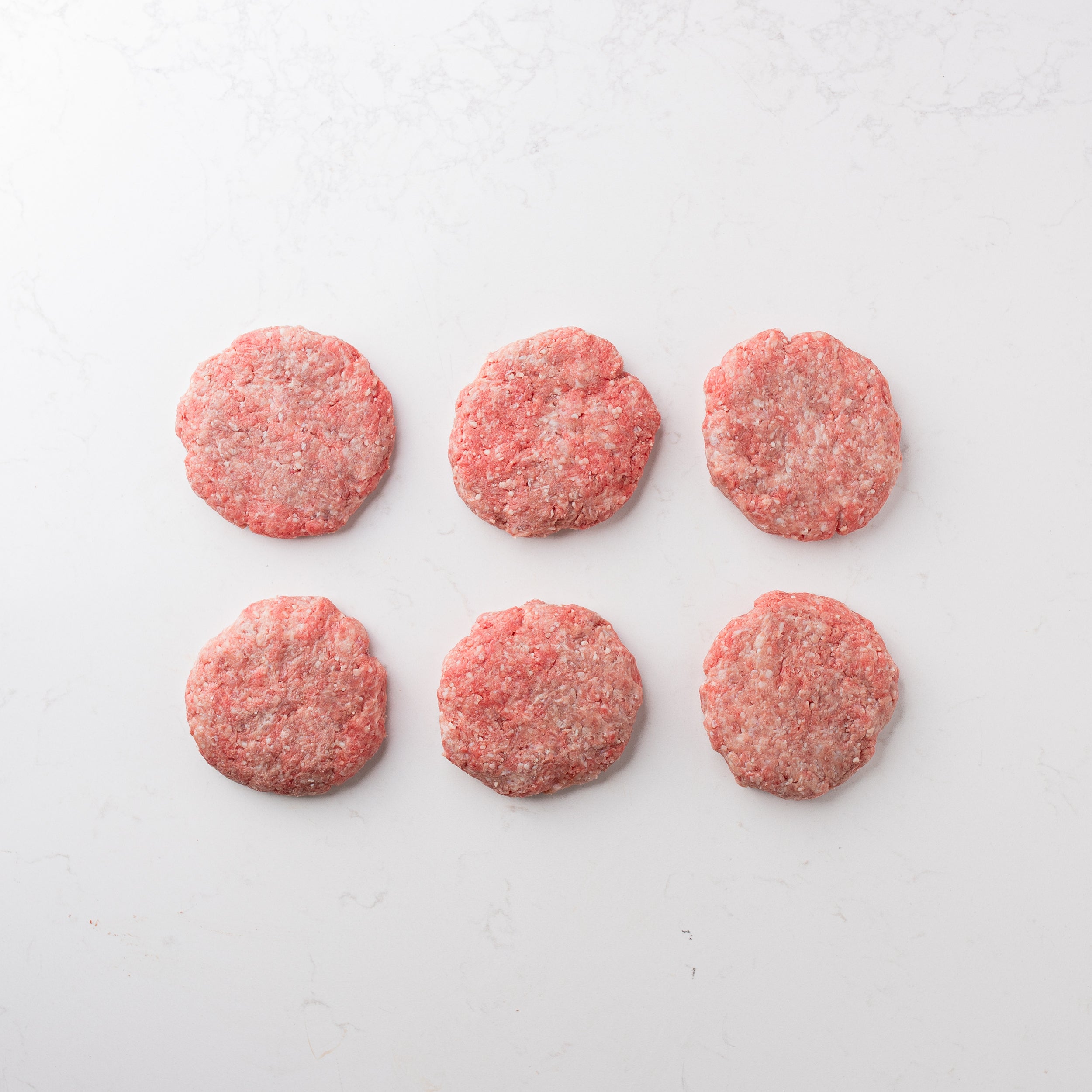 Six raw hamburger patties arranged in two rows on a white surface.