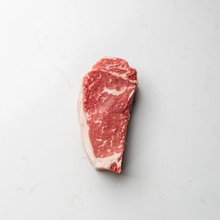 A close-up view of a fresh, local, and natural New York striploin steak, displayed at the butcher shoppe